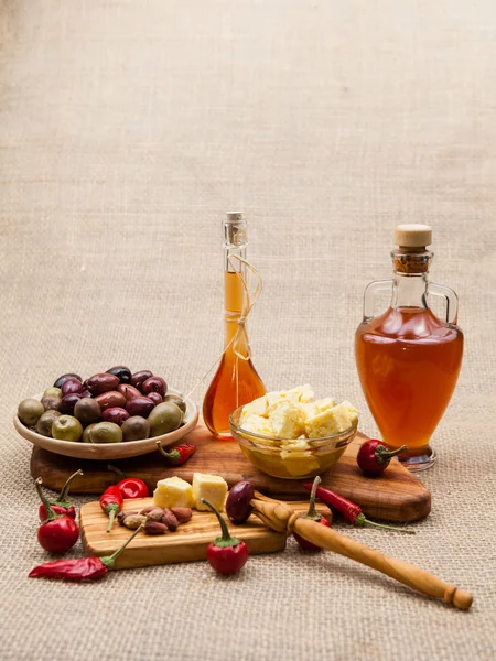 Composición con madera de olivo, aceitunas, trozos de queso en aceite de oliva, vinagre y especias y textura de arpillera —  Fotos de Stock