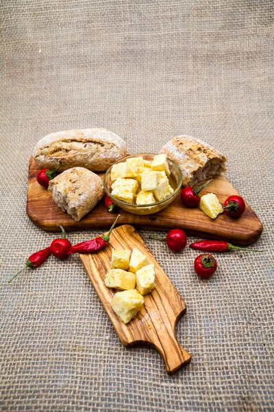 Composizione con legno di ulivo, pezzi di formaggio in olio d'oliva, pane e peperoncini piccanti con texture di iuta — Foto Stock