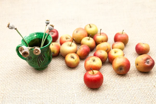 Pequeñas manzanas rojas y taza de cerámica con semillas de amapola con textura de arpillera en el fondo —  Fotos de Stock
