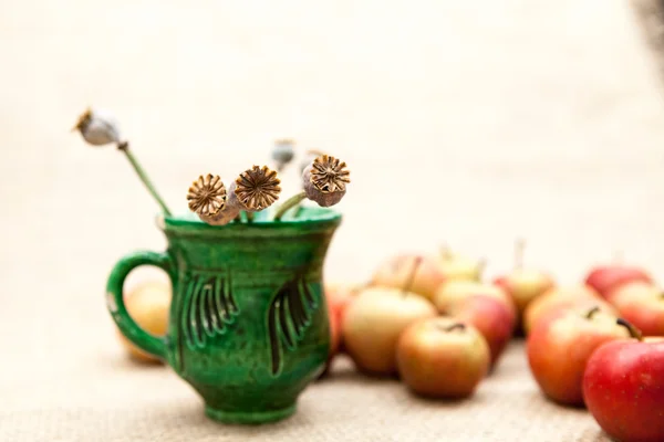 Pequeñas manzanas rojas y taza de cerámica con semillas de amapola con textura de arpillera en el fondo —  Fotos de Stock