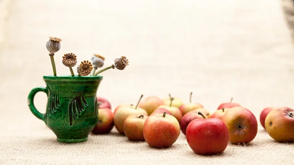 Pequeñas manzanas rojas y taza de cerámica con semillas de amapola con textura de arpillera en el fondo —  Fotos de Stock