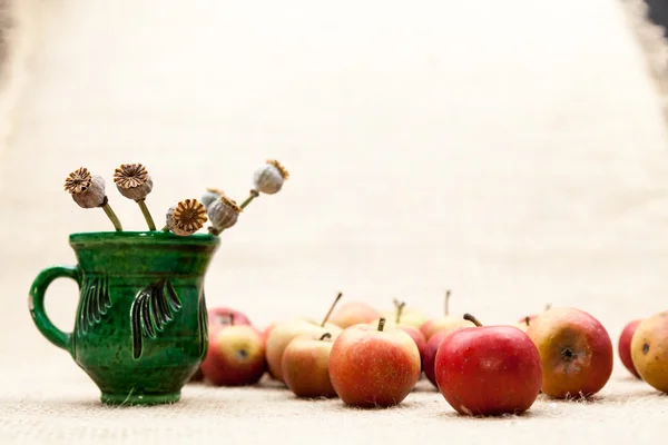 Pequeñas manzanas rojas y taza de cerámica con semillas de amapola con textura de arpillera en el fondo —  Fotos de Stock