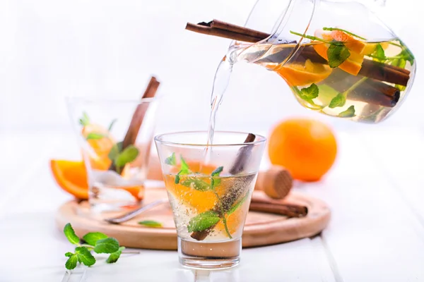 Thee met sinaasappel, munt en kaneel op houten witte achtergrond — Stockfoto