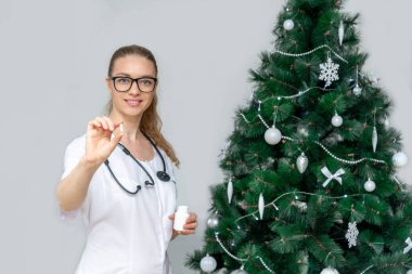 Kadın bir doktor Noel ağacının arkasında haplar tutuyor. Noel tatilleri ve yeni yıl boyunca aşırı yemekten kaynaklanan sindirim tedavisi. Baş ağrısı için eve ilk yardım. Çevrimiçi danışma