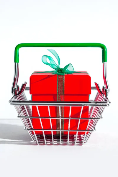 Mały koszyk spożywczy z czerwonym pudełkiem na białym, izolowanym tle. Kreatywne świąteczne zakupy online. Sprzedaż wakacyjna i rabaty na nowy rok i czarny piątek. Handel. Twarde cienie. — Zdjęcie stockowe