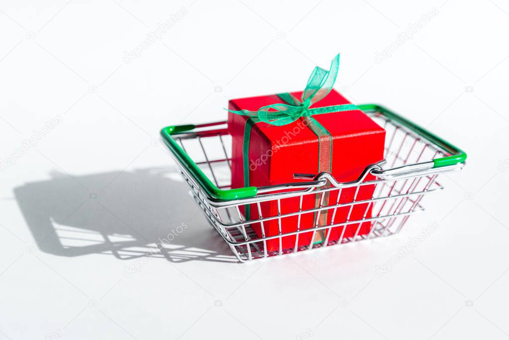 Grocery basket with red gift box on white isolated background. Christmas shopping online. Copy space. Holiday sales and discounts on new year and black Friday. Trading business. Space for text.