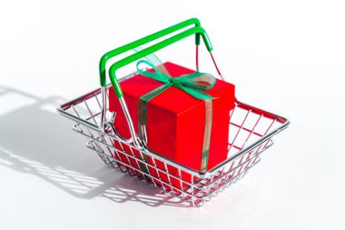 Beyaz izole edilmiş arka planda kırmızı hediye kutusu olan küçük bir market sepeti. İnternetten yaratıcı Noel alışverişi. Yılbaşı ve Kara Cuma 'da tatil satışları ve indirimler. Ticaret işi. Sert gölgeler.
