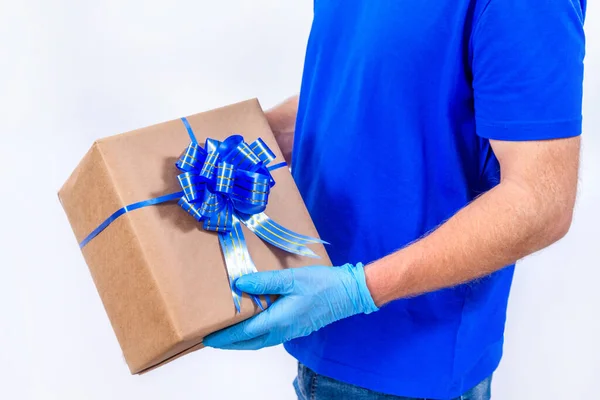 Livraison à distance sans contact de cadeaux pendant la pandémie de coronavirus. Ferme là. Courier main dans des gants médicaux de protection tient une belle boîte-cadeau avec un arc sur un fond blanc. — Photo
