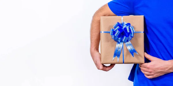 Banner. Manos de cerca. El mensajero en uniforme azul sostiene la caja de regalo con un lazo. Feliz año nuevo y feliz Navidad. Entrega remota sin contacto segura de regalos navideños durante coronavirus. Copiar espacio. — Foto de Stock