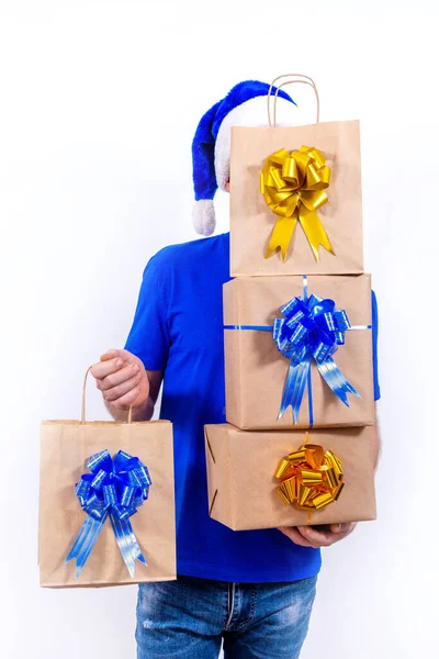 Feliz mensajero en uniforme azul y sombrero de Santa tiene muchas cajas de regalo y paquetes. Feliz año nuevo y feliz Navidad. El hombre sonríe. Entrega remota sin contacto segura de regalos de vacaciones durante coronavirus. —  Fotos de Stock