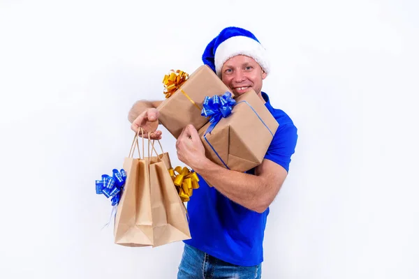 Joyeux coursier en uniforme bleu et chapeau de Père Noël détient de nombreuses boîtes-cadeaux et des paquets. Bonne année et joyeux Noël. Un homme sourit. Livraison sécurisée à distance sans contact de cadeaux de vacances pendant le coronavirus. — Photo