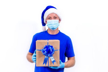Mavi üniformalı, koruyucu tıbbi maskeli, eldivenli ve Noel Baba şapkalı bir kurye. Mutlu yıllar ve mutlu Noeller. Coronavirus sırasında tatil hediyelerinin güvenli bir şekilde teslim edilmesi.