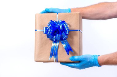 Coronavirüs salgını sırasında uzak mesafeden tatil hediyelerini güvenli bir şekilde teslim etmek. Kapatın. Koruyucu tıp eldivenleri içindeki kurye elinde beyaz arka planda fiyonklu güzel bir hediye kutusu var..