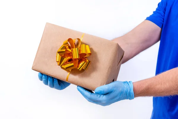 Безпечна дистанційна доставка святкових подарунків під час пандемії коронавірусу. Близько. Кур'єрська рука в захисних медичних рукавичках тримає красиву подарункову коробку з бантом на білому тлі . — стокове фото