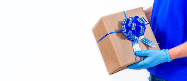 班纳在大肠病毒大流行期间，安全、无接触性地远程运送节日礼物。带着防护手套的信使手拿着漂亮的礼品盒，上面有一个白色背景的蝴蝶结。复制空间. — 图库照片