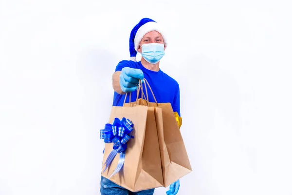 青い制服 保護医療用マスク サンタクロースの帽子の宅配便はギフトバッグを保持しています 新年と陽気なクリスマス コロナウイルス中の休日の贈り物の安全な非接触リモート配信 — ストック写真