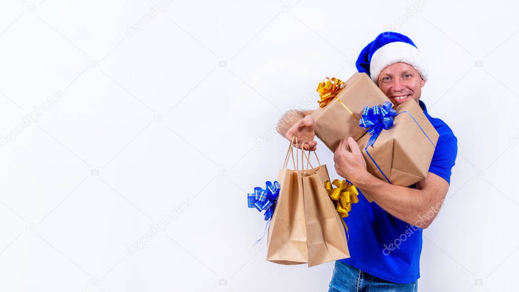 Banner. Happy courier in a blue uniform and Santa hat holds many gifts in his hands. New year and merry Christmas. Man smiles. Secure contactless remote delivery of holiday gifts during coronavirus.