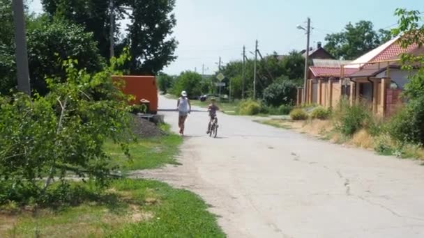 Starší sestra učí mladšího bratra jezdit na kole. Dívka pomáhá malému chlapci naučit se jezdit. Školní prázdniny a hry ve vesnici s babičkou. Letní zábava s přáteli. — Stock video