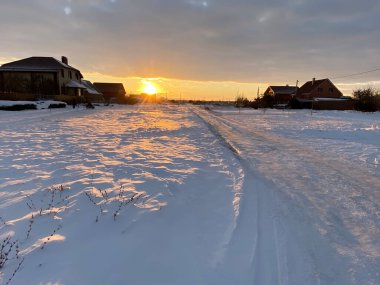 Rus köyünde kar yolu batan güneş manzaralı. Kar çok güzel parlıyor ve güneş ışınlarını yansıtıyor. Taşra yerleşimi. Rusya, Rostov bölgesi, Volgodonsk.