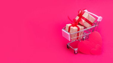 Kırmızı-pembe arka planda hediye kutuları olan küçük bir market arabası. Sevgililer Günü 'nde, Noel' de ve doğum gününde sevgiyle hediye ver. İnternetten alışveriş. Tatil satışları ve indirimler. Perakende ve toptan alım.
