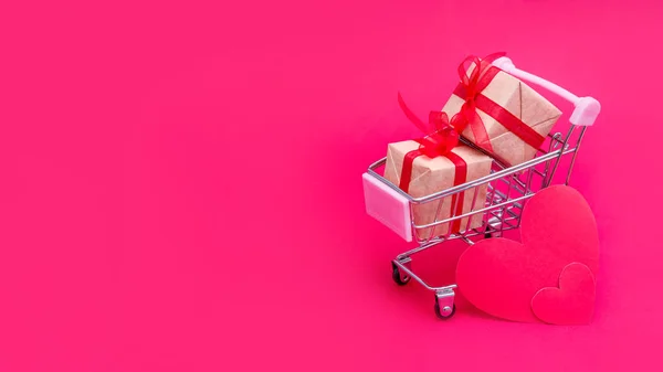 빨간 - 핑크 배경에 선물 상자가 있는 작은 식료품 카트. 발렌타인 데이, 크리스마스, 생일에 사랑으로 선물을 주 세요. 온라인 쇼핑. 휴일 매상고와 할인가 입니다. 소매 및 도매상 구매. — 스톡 사진