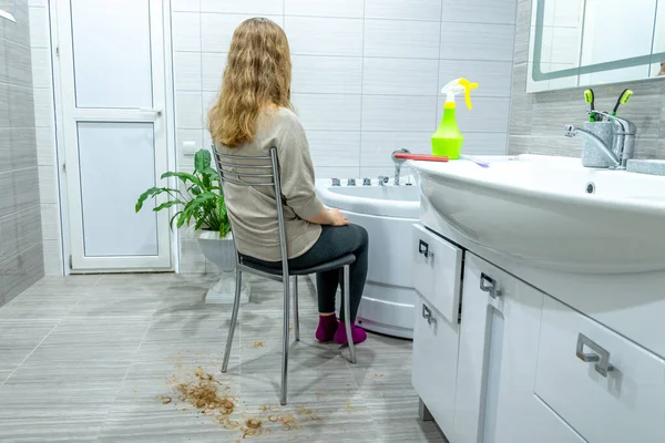 Home salon haircut during quarantine. Girl with long hair is sitting on chair in the bathroom, her hair cut off on floor around her. closed beauty salons due to pandemic. Home pastime, leisure.