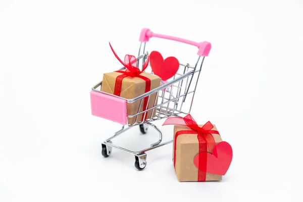 白い背景にギフトボックス付きの小さな食料品のカート。バレンタインデー、クリスマス、誕生日に愛を込めて贈り物をしましょう。オンラインショッピング。休日の販売と割引。小売・卸売の購入. — ストック写真