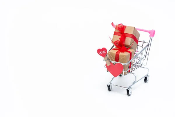 Malý nákupní vozík s dárkovými krabicemi na bílém pozadí. Dát dárky s láskou na Valentýna, Vánoce a narozeniny. Nakupování online. Dovolenkový prodej a slevy. Maloobchodní a velkoobchodní nákupy. — Stock fotografie
