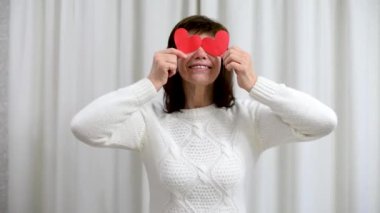Çılgın yetişkin yaşlılar Sevgililer Günü 'nü kutluyor. Kadın, kırmızı sevgililer günü kartlarıyla gözlerini kapar ve gülümser. Romantik ilişkiler, aşk ve emeklilikte flört. Yaşlıların yaşam tarzı.