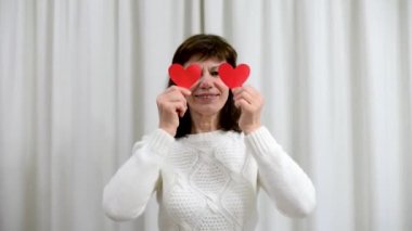Çılgın yetişkin yaşlılar Sevgililer Günü 'nü kutluyor. Kadın, kırmızı sevgililer günü kartlarıyla gözlerini kapar ve gülümser. Romantik ilişkiler, aşk ve emeklilikte flört. Yaşlıların yaşam tarzı.