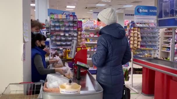 保護マスクの女性はスーパーマーケットのレジカウンターで彼女の購入のために支払う キャッシャーパンチ製品 コロナウイルスのパンデミック時に食料品店を訪問 ロシアヴォルゴンドンスク2021年2月12日 — ストック動画