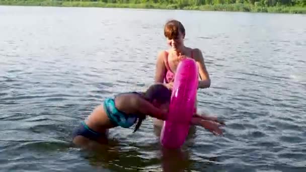 Chica feliz y la mujer juegan en el agua en la playa en verano. La hija adolescente salta en un círculo inflable y nada a través de él. Fines de semana y vacaciones escolares. Concepto de vacaciones, diversión y gente. — Vídeos de Stock