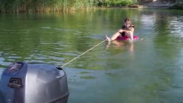 Funny teenage girl is sitting in scuba mask, life jacket on swimming circle in sea and holding on to rope. Dad rides his daughter in tow on water by tying an inflatable circle to motor boat. Vacation. — Stock Video
