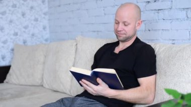 Oturma odasındaki koltukta oturan orta yaşlı traşsız adam dikkatlice kitap okuyor. Karantina ve salgın sırasında yeni başlangıçlar. Uzaktan eğitim. Evde öğrenim. İlginç edebiyat.