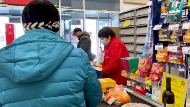 保護マスクと手袋の女性のレジ係はチェックアウト時にスーパーマーケットで食品を販売しています。隔離およびパンデミックコロナウイルス中の販売者および購入者の保護。ロシア、ヴォルゴドンスク2021年2月24日. — ストック動画