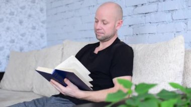 Oturma odasındaki koltukta oturan orta yaşlı traşsız adam dikkatlice kitap okuyor. Karantina ve salgın sırasında yeni başlangıçlar. Uzaktan eğitim. Evde öğrenim. İlginç edebiyat.