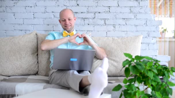 Love in lockdown. Adult elegant man in shirt with bow tie shows hands shape of heart on romantic virtual date via call. Happy man talking to woman on video chat on Valentines Day in self-isolation. — Stock Video