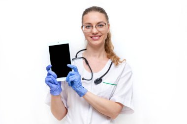 Steteskoplu beyaz önlüklü kadın doktor onu beyaz arka planda izole edilmiş elektronik tabletle tutuyor. Genç, güzel bir kadın hastane sağlık görevlisi kameraya bakıyor ve gülümsüyor. Model