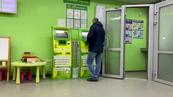 Tıbbi maskeli adam bankadaki elektronik terminalden ödeme yapıyor. Koronavirüs salgını sırasında bankayı ziyaret etmek. Boş bir ofis. Halka açık bir yerde güvenlik ve mesafe. Volgodonsk, Rusya, 20 Mart 2021. — Stok video