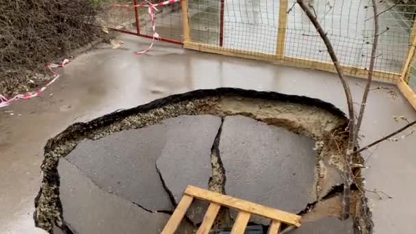 Katastrofalne zniszczenie drogi asfaltowej. Głębokie dziury w płótnie. Duży dół otoczony płotem. Słaba konstrukcja technologii budowy autostrad i chodników. Zniszczona droga. — Wideo stockowe