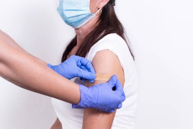Doktor ya da hemşire, aşı ya da aşıdan sonra hastanın omzuna yara bandı yapıştırır. Yakın plan. Grip aşısı, salgın koronavirüs. İnsanların virüse karşı dokunulmazlıklarının zorunlu olarak önlenmesi