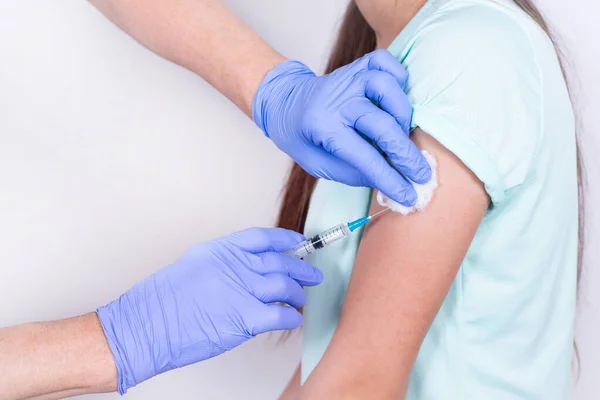 Vrouwelijke arts of verpleegkundige geven schot of vaccin aan patiënten schouder - jong meisje. Een close-up. Vaccinatie tegen griep, pandemisch coronavirus. Verplichte preventie van mensen voor immuniteit tegen het virus. Stockfoto