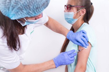 Bayan çocuk doktor ya da hemşire hastalara iğne ya da aşı yapıyor. Genç kız. Grip aşısı, salgın koronavirüs. İnsanların virüse karşı dokunulmazlıklarının zorunlu olarak önlenmesi.