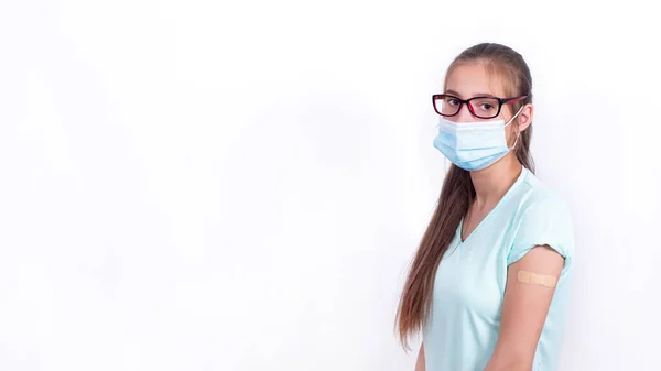 Teenage girl in mask with Band-Aid on shoulder after vaccination against coronavirus or flu. Mandatory prevention for young people for immunity from virus. person isolated on white background. Banner. Stockafbeelding