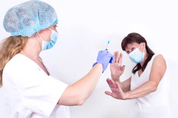 Vaksinasi paksa. Pasien wanita menolak suntikan. Dokter wanita memegang jarum suntik di tangan untuk memvaksinasi pasien. Pencegahan terhadap pandemi virus, coronavirus. Vaksinasi wajib bagi masyarakat. Stok Gambar Bebas Royalti