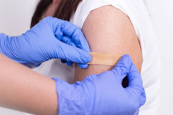 Dokter atau perawat lem Band-Aid pada pasien bahu setelah suntikan atau vaksinasi. Close-up. Vaksinasi terhadap flu, pandemi coronavirus. Pencegahan wajib terhadap orang yang kebal dari virus.. Stok Lukisan  