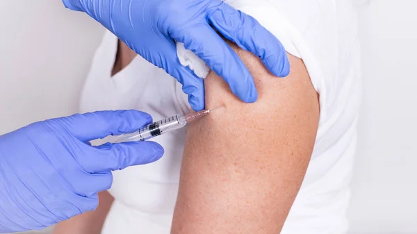 女性医師または看護師が肩に注射またはワクチンを投与する。接近中だ。インフルエンザ、パンデミックコロナウイルスに対するワクチン。ウイルスからの免疫のための人々の必須予防. ロイヤリティフリーのストック画像
