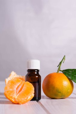 Koyu cam bir şişe ve parlak turuncu mandalinalar içindeki temel yağ..
