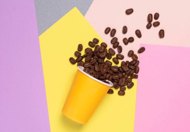 Portakal rengi tek kullanımlık kağıt bardak ve arka planda çok renkli blokların üst görüntüsünde kavrulmuş kahve çekirdekleri. Parlak kartpostal