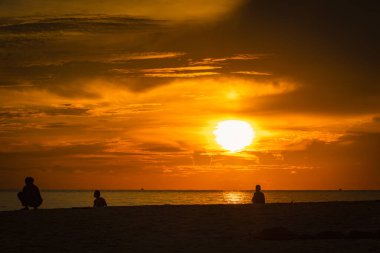 Sahilde güneşin doğuşunu izleyen insanların silueti.